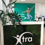 Het Xtra interim & selectie kantoor in Turnhout in beeld. Je ziet een balie met moswand en Xtra logo. Op de achtergrond een grote foto van een mevrouw die springt en gelukkig is. Opschrift: Hou van maandag